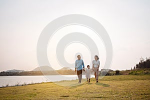 Happy family in the park sunset light. family on weekend running together in the meadow with river Parents hold the child hands.