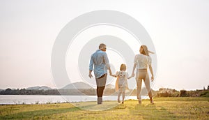 Happy family in the park sunset light. family on weekend running together in the meadow with river Parents hold the child hands.