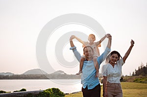 Happy family in the park sunset light. family on weekend running together in the meadow with river Parents hold the child hands.