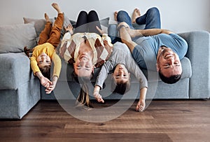 Happy family people and their kids in casual clothes are lying upside down on their backs on grey sofa