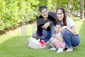 Happy family with pet has fun together in summer green garden. Father, mother and kid play with fluffy white Pomeranian dog, mom