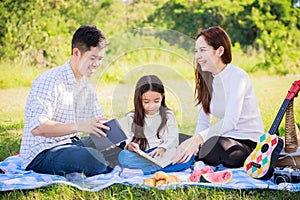 Happy family picnic. Asian parents Father, Mother and little girl reading a book and have fun and enjoyed ourselves together