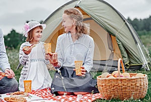 Happy family on picnic at camping. Mother and daughter eating near a tent in meadow or park