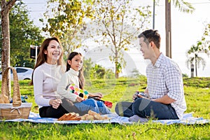 Happy family picnic. A little girl playing ukulele with her parents Father, Mother during picnicking on a picnic cloth on a