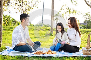 Happy family picnic. A little girl playing ukulele with her parents Father, Mother during picnicking on a picnic cloth on a