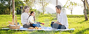 Happy family picnic. A little girl playing ukulele with her parents Father, Mother during picnicking on a picnic cloth on a