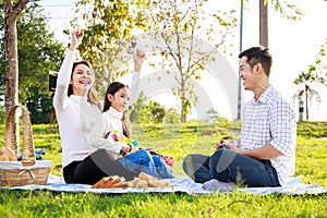 Happy family picnic. A little girl playing ukulele with her parents Father, Mother during picnicking on a picnic cloth on a