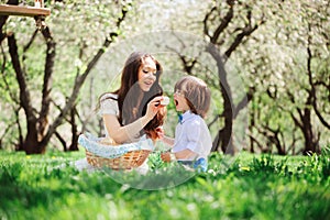 Happy family on picnic for mothers day. Mom and toddler son eating sweets outdoor in spring