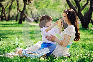 Happy family on picnic for mothers day. Mom and toddler son eating sweets outdoor in spring