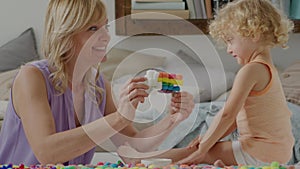 Happy family play at home, mom with little girl together build and draw colorful shapes using educational toys to stimulate