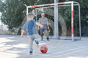 Happy family playing football. Back view of boy kicking soccer ball. Grandfather soccer goalkeeper warding the football