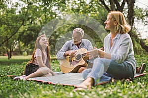 Happy family playing guitar in their green park garden.