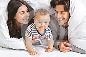 Happy family playing hiding under blanket in bed