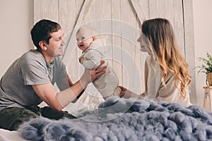 Happy family playing at home on the bed. Lifestyle capture of mother, father and baby
