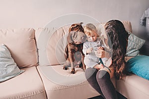 Happy family playing at home with dog. Mother and baby boy eating cookies