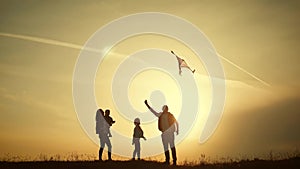 Happy family playing with a kite while on meadow, sunset, in summer day. Funny family time. Happy little girl launch a