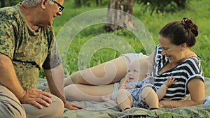 Happy family playing with a little toddler boy in an summer park with beautiful grass. Mother, baby, grandfather