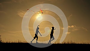 Happy family playing outdoors, flying kite flying. Silhouette of children with a kite at sunset. Team work, team play