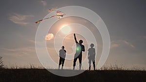 Happy family playing outdoors, flying kite flying. Silhouette of children with a kite at sunset. Team work, team play