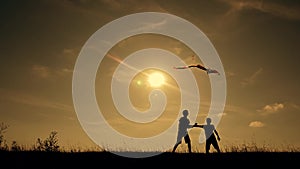 Happy family playing outdoors, flying kite flying. Silhouette of children with a kite at sunset. Team work, team play