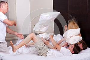 Happy family playing with pillows on the bed