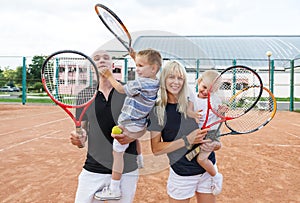 Happy family playing tennis holding rackets at the court