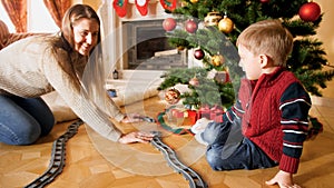 Happy family playing with toy railroad on Christmas morning. Child receiving presents and toy on New Year or Xmas