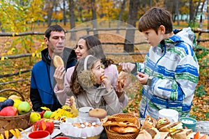 Happy family portrait in autumn city park. People are sitting at the table, eating and talking. Posing against the background of