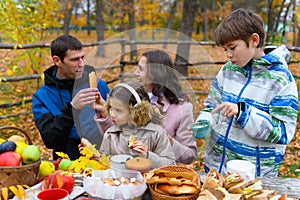Happy family portrait in autumn city park. People are sitting at the table, eating and talking. Posing against the background of