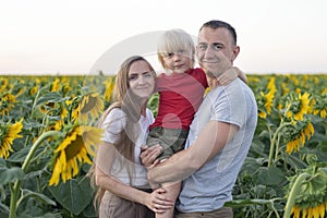 Happy family portrait on sunflower field background: mom dad and son. Summer vacation