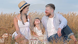 Happy family portrait, young couple sits together close to their child girl daughter in open air outings in harvest