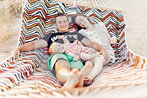 Happy family portrait, young hipster father and mother lying in a hammock with their baby daughter, summer vacation family trip