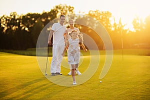 Happy family posing on a golf course on a sunset background. The girl smiles and runs towards the camera