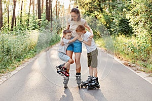 Happy family posing in summer park, mother and two her sons roller skating together, woman spending weekend with her children in