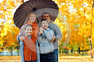 Happy family posing under umbrella, playing and having fun in autumn city park. Children and parents together having a nice day.