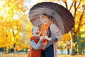 Happy family posing under umbrella, playing and having fun in autumn city park. Children and parents together having a nice day.