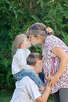 Happy family. Pregnant mother with her husband and son in the park. Mum kisses the son and dad kissing mums belly