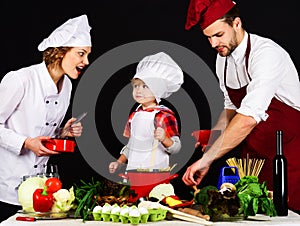 Happy family preparing healthy food together in kitchen. Adorable son in chef hat with parents cooking together at home