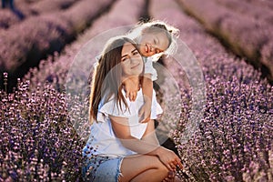 Happy family in purple lavender field. young beautiful mother and child Girl enjoy walking blooming meadow on summer day