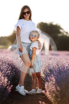 Happy family in purple lavender field. young beautiful mother and child Girl enjoy walking blooming meadow on summer day