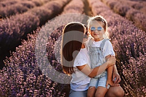 Happy family in purple lavender field. young beautiful mother and child Girl enjoy walking blooming meadow on summer day