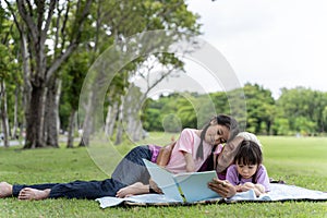 Happy family read books together and lying on green grass in public park. Little girl kid learning with grandfather in outdoors