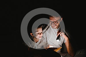 Happy family reading bedtime story under blanket in evening. Father and son spend time together. Father's Day