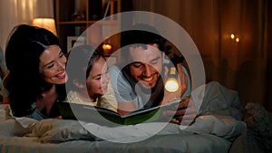 Happy family reading book in bed at night at home