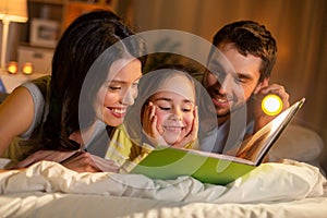 Happy family reading book in bed at night at home