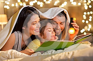 Happy family reading book in bed at night at home