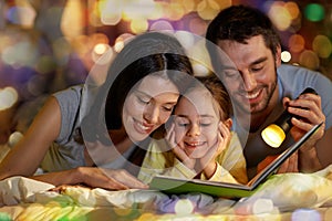 Happy family reading book in bed at night at home