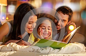 Happy family reading book in bed at night at home