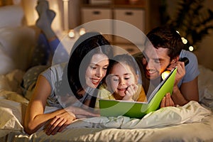 Happy family reading book in bed at night at home