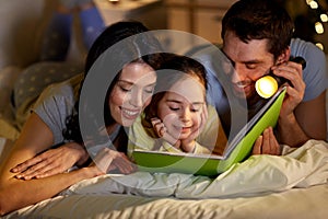 Happy family reading book in bed at night at home